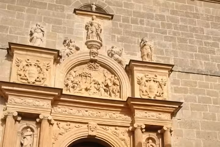 Visitors on guided tour of Huete Monumental admire ornate Baroque church portal and carved stone facade