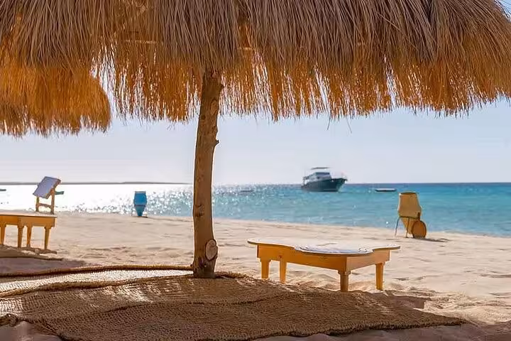 Shaded beach loungers and thatched umbrella on Hula Hula Island, Hurghada with yacht and Red Sea views