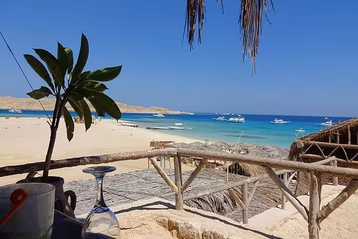 Hula Hula Island beach view with palm shade, turquoise Red Sea lagoon and boats on day trip with lunch