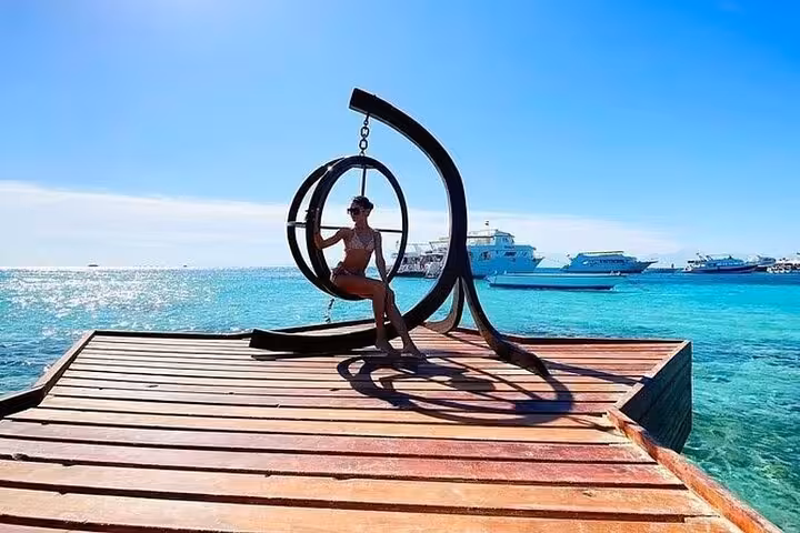 Relaxing on Hula Hula Island pier swing over turquoise Red Sea, Hurghada day trip with lunch and water sports