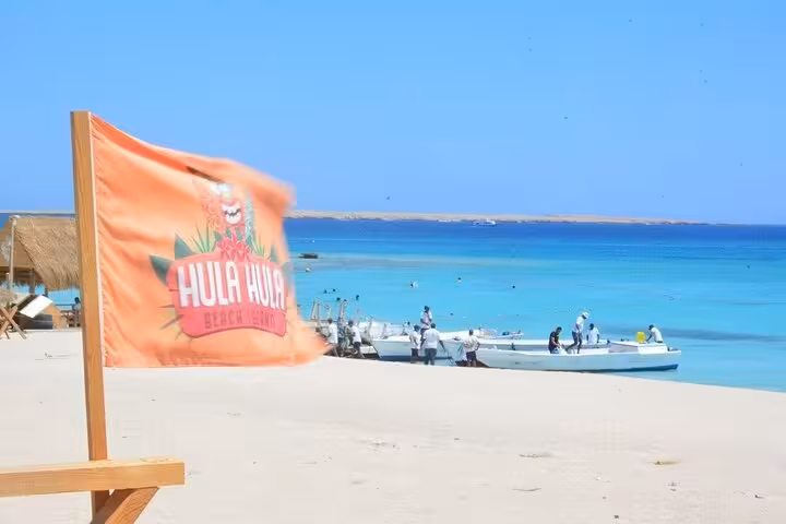 Hula Hula Island flag by the shore with boats in crystal Red Sea, pickup for lunch and water sports adventure