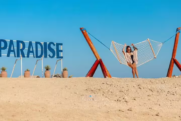 Traveler relaxing in beach hammock by Paradise sign on Hula Hula Island, VIP boat trip from Hurghada