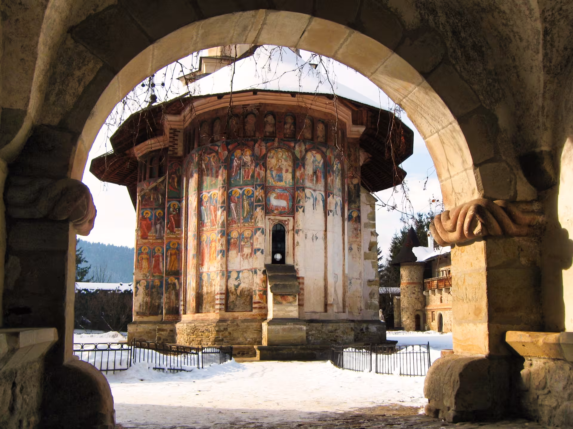 Stunning painted exterior frescoes of Humor Monastery seen through stone arch on a 2-day Bucovina tour in winter