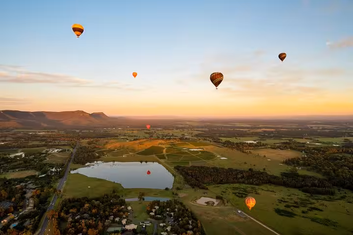 Hot air balloons floating over the picturesque landscape of Hunter Valley at sunrise, ideal for winery tours.