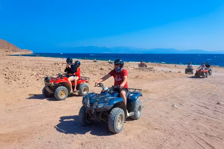 Riders on ATV quad bikes along Hurghada Red Sea coast, desert track with mountains on the horizon
