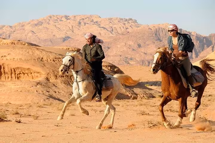 Two riders galloping horses across Hurghada desert landscape, part of one-hour beach horse riding tour with transfer