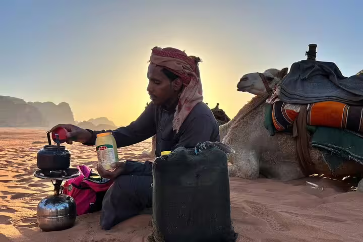 Bedouin guide brewing tea beside camel at sunset during Hurghada desert safari with camel ride and dinner