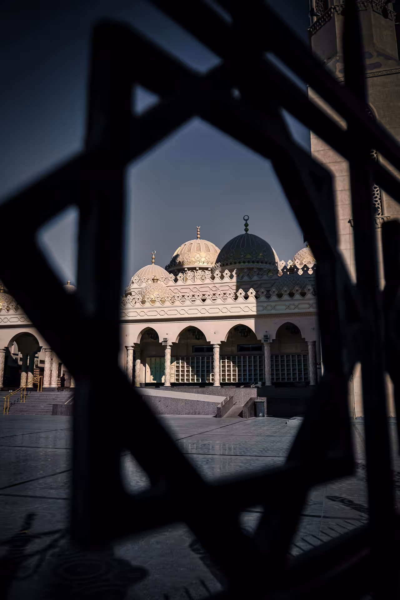 Mosque domes and arched courtyard viewed through ornate iron gate in Hurghada city