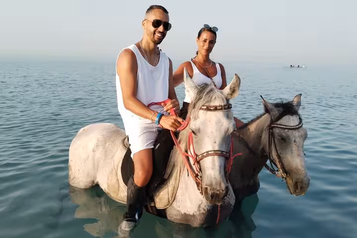 Couple riding horses in shallow Red Sea water in Hurghada with optional swimming beach horseback tour