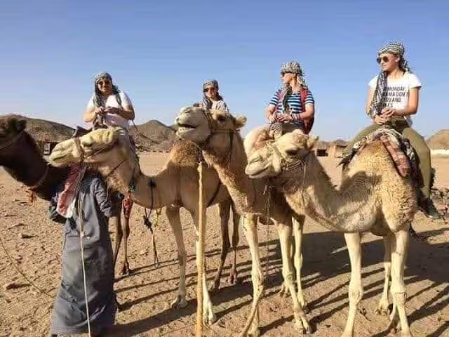 Camel ride during Mega Safari in Hurghada desert, tourists wearing Bedouin scarves with mountains in the background