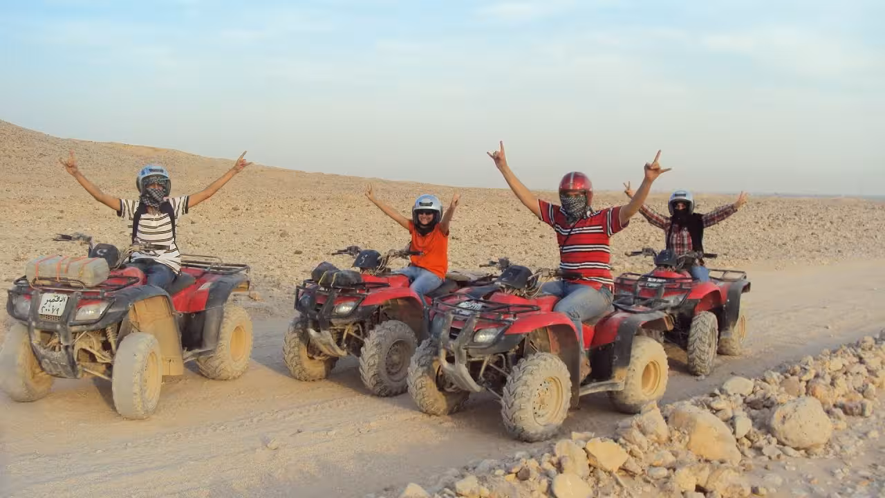 Guests on ATVs in Hurghada desert raising arms, adrenaline quad ride before jeep safari dinner and stargazing