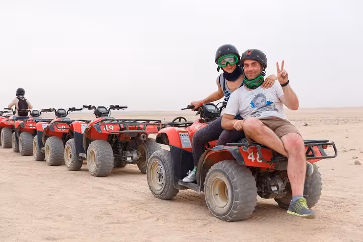 Couple posing on ATV in Hurghada desert, quad bike tour lineup with helmets, goggles, transfer and BBQ