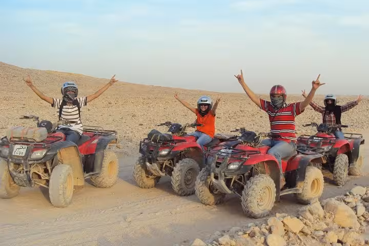 Group on red quad bikes celebrating on Hurghada desert ATV safari with helmets, transfers and BBQ dinner