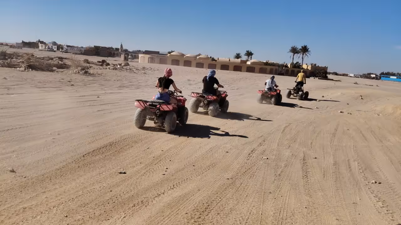 Four riders on red quad bikes racing through sandy desert terrain in Hurghada with palm trees in background