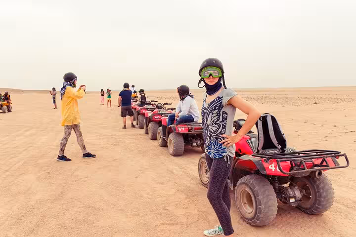 Woman rider beside quad bike in Hurghada desert, guided ATV safari lineup with helmets, transfer and BBQ