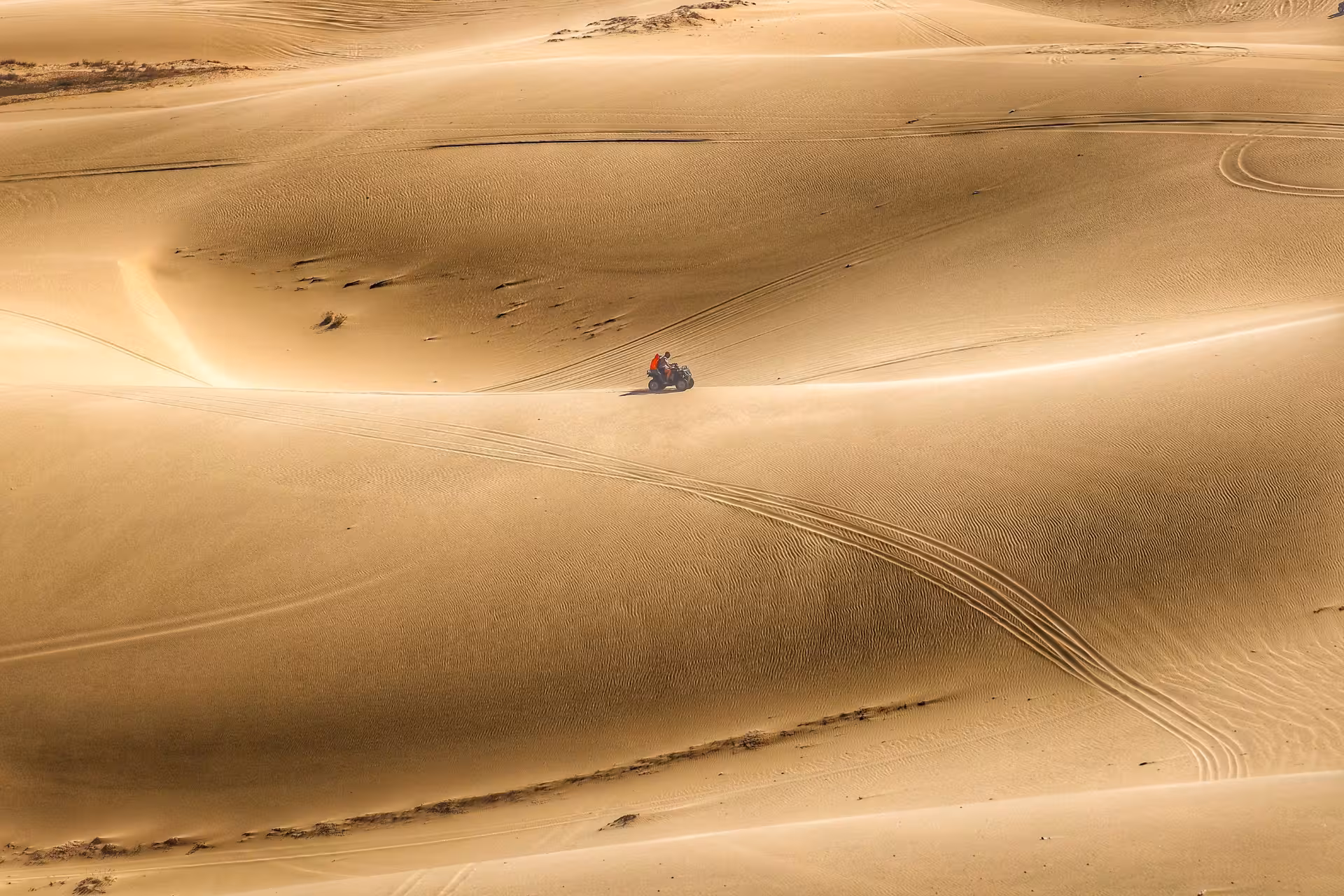 Quad bike rider in orange jacket navigating vast golden sand dunes in Hurghada desert