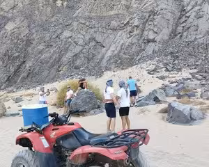 Tourists standing near red quad bike on sandy desert terrain with rocky cliffs in Hurghada