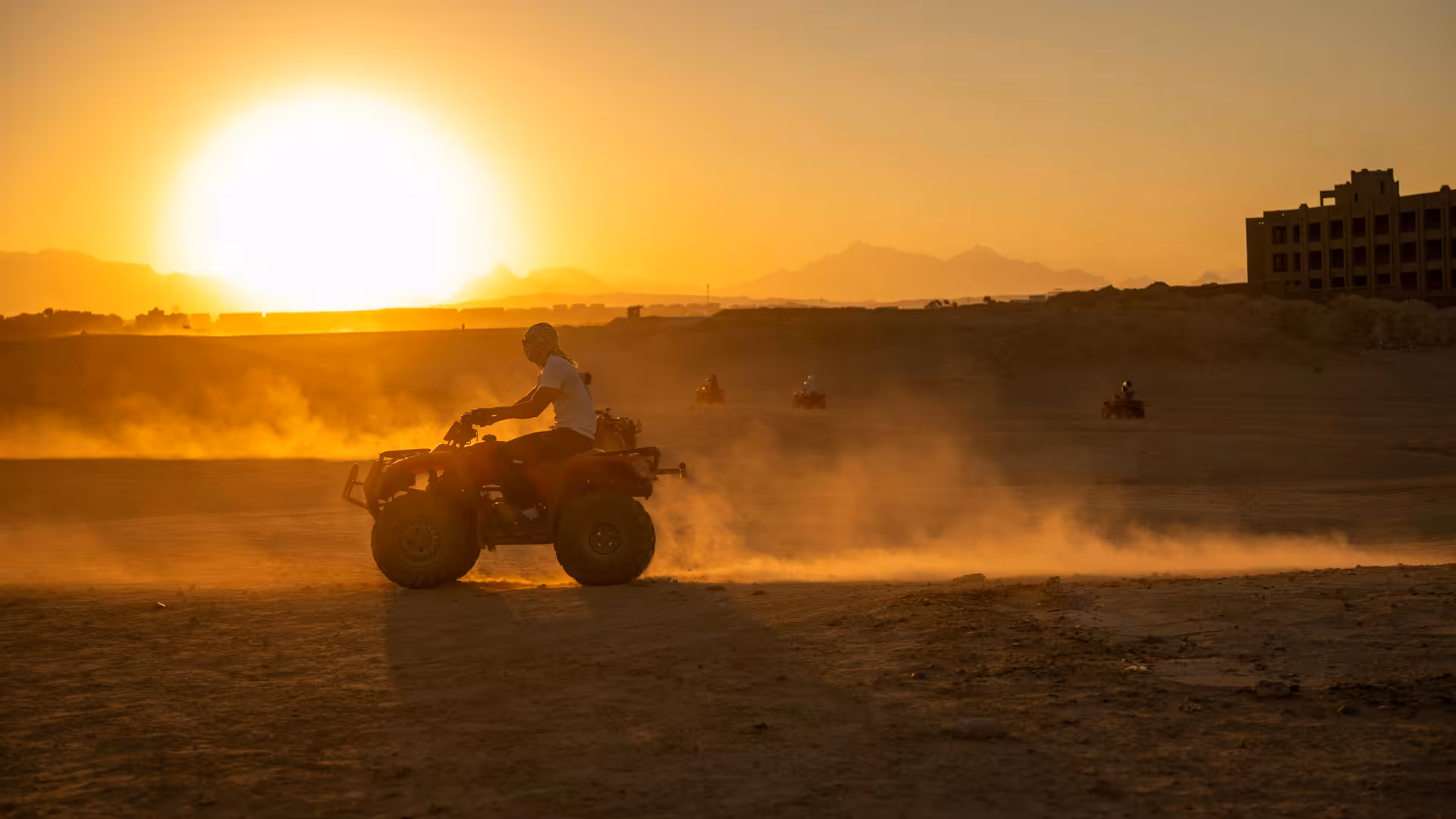Quad bikers riding through dusty desert at golden sunset near Hurghada with mountains in background