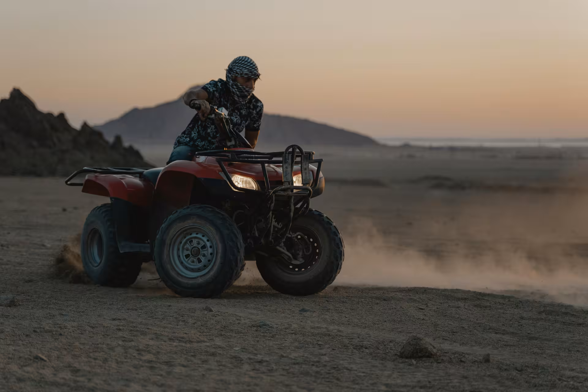 Rider on red quad bike kicking up dust in Hurghada desert at sunset