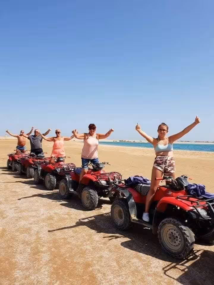 Group of tourists standing on red quad bikes on sandy desert beach near Hurghada coastline