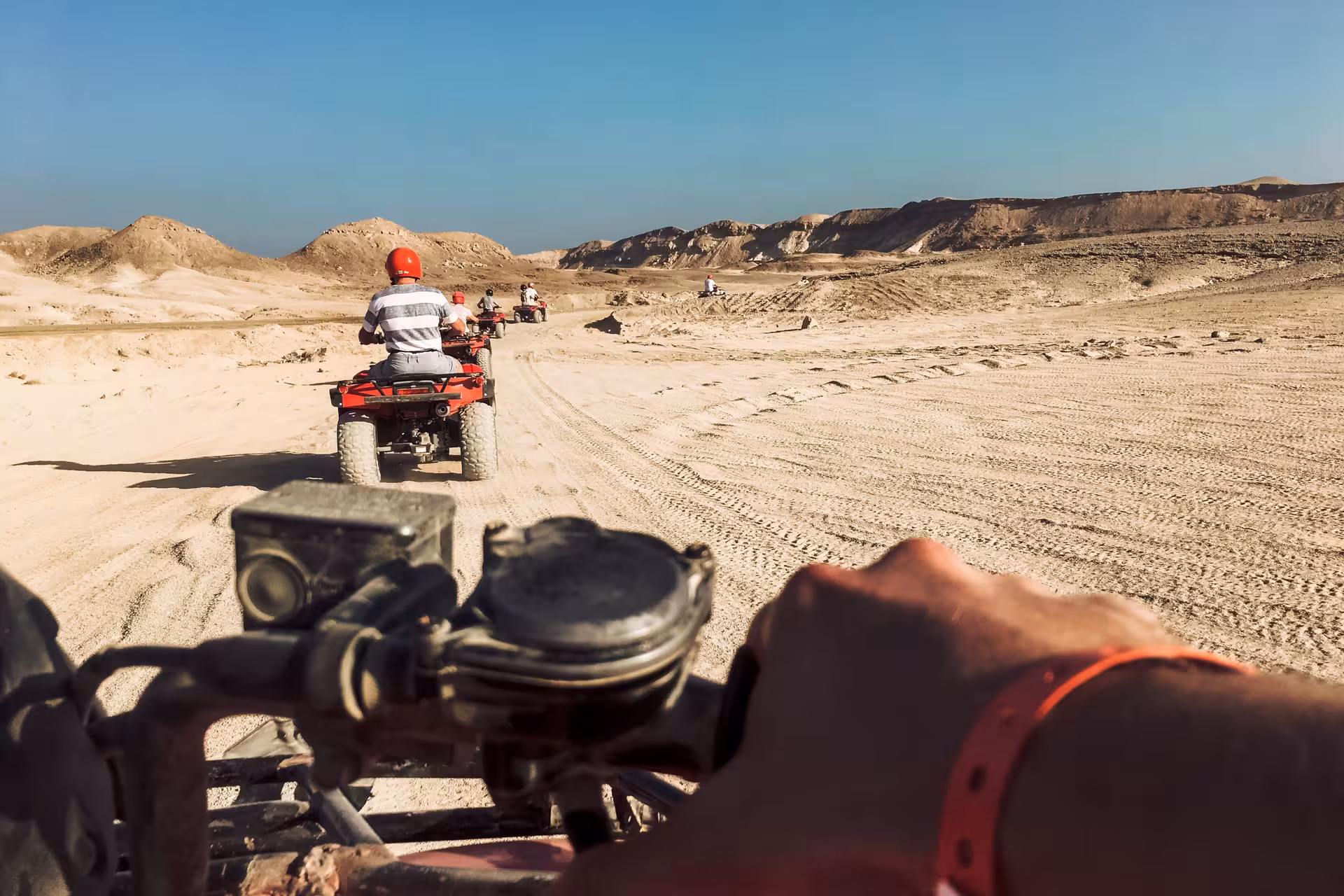 Group of riders on red quad bikes riding through sandy desert terrain in Hurghada, Egypt