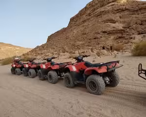 Five red quad bikes lined up in a row on desert sand near rocky cliffs in Hurghada