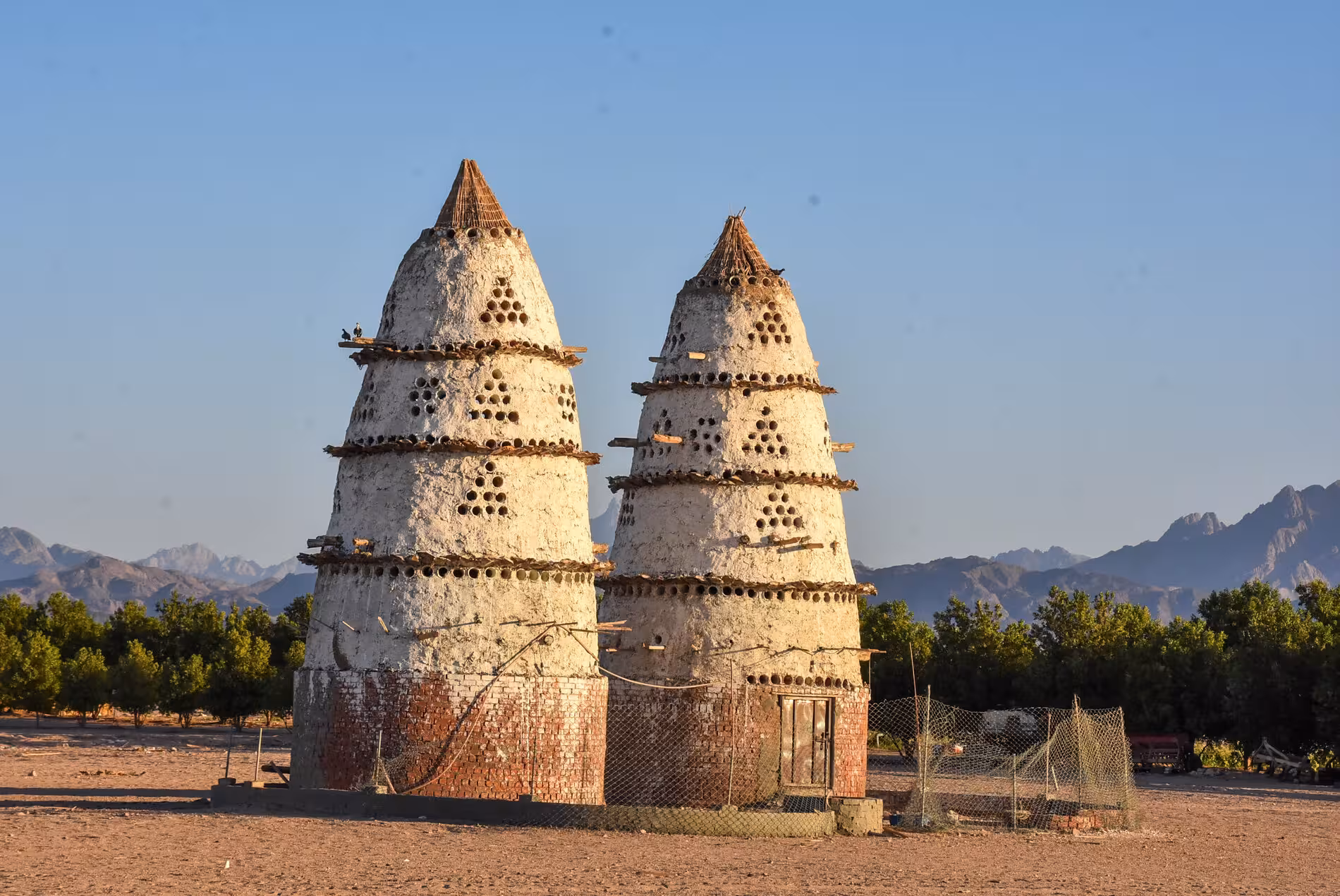Twin ancient mud-brick pigeon towers with circular holes in Egyptian desert with mountains backdrop