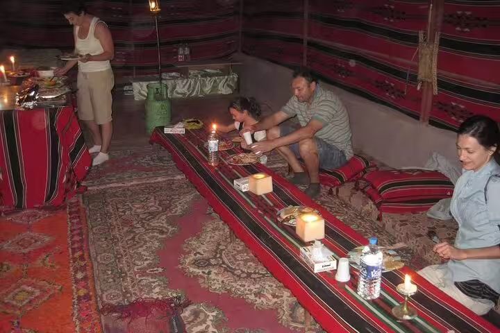 Guests enjoying Bedouin dinner inside desert tent after sunset quad bike safari and camel ride, candlelit seating