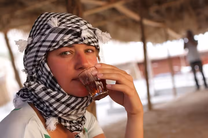 Guest in keffiyeh sipping Bedouin tea at Hurghada desert camp on 6-hour jeep safari with BBQ dinner and show
