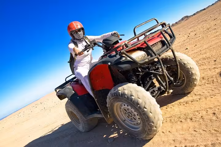 Rider on quad bike racing across Hurghada desert sands during 6-hour jeep safari with BBQ dinner and show