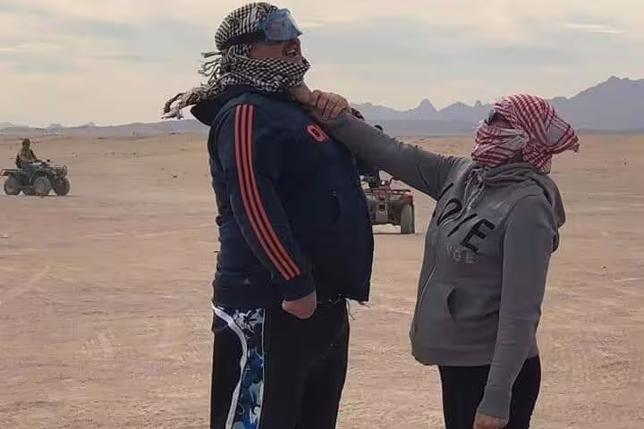 Guests in desert scarves pose during sunset quad bike desert safari, with ATVs in the background