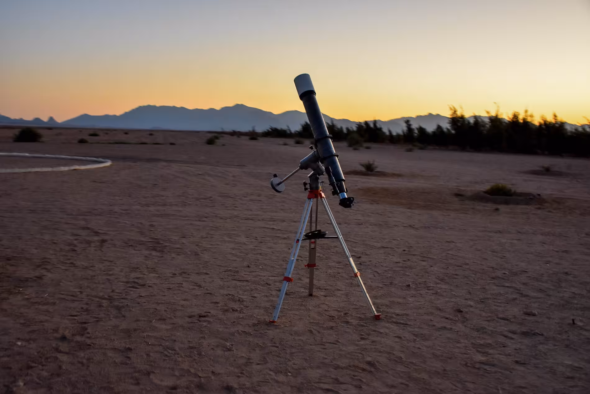 Telescope on tripod in desert at sunset with mountain silhouettes, Hurghada stargazing tour