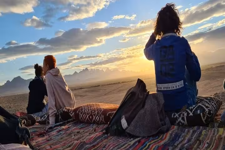 Guests relax on Bedouin rugs at sunset in Hurghada desert, before stargazing jeep tour and optional ATV
