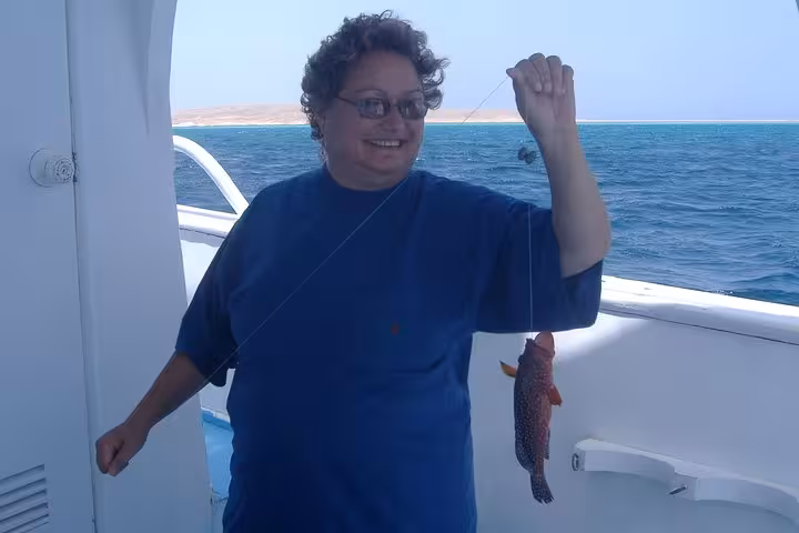Happy angler holding a reef fish on board, Red Sea fishing tour from Hurghada with scenic coastline views