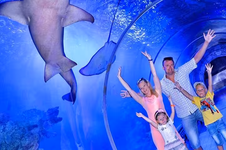 Family posing in Hurghada Grand Aquarium underwater tunnel with sharks, discovery tour tickets and transfers