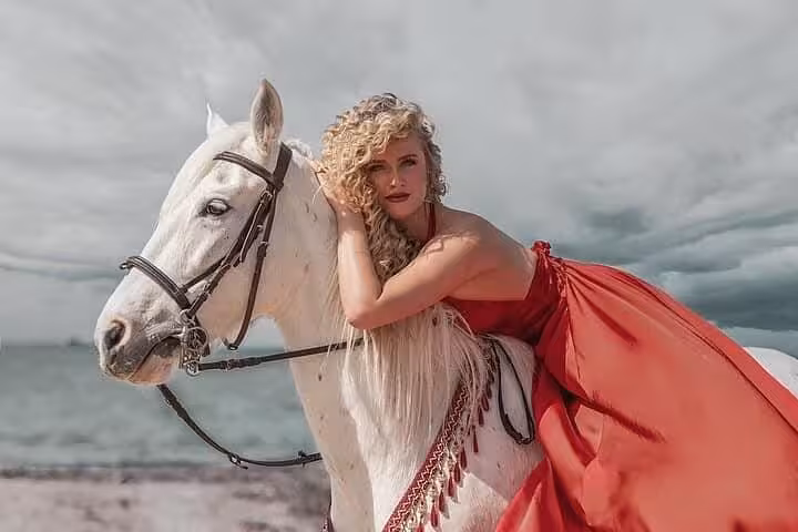Woman in red dress posing on white horse by the sea on Hurghada desert and beach horse riding tour
