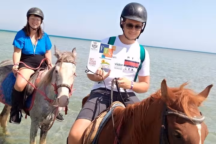 Riders in helmets pose on horseback in shallow Red Sea water during Hurghada desert and sea horse riding tour