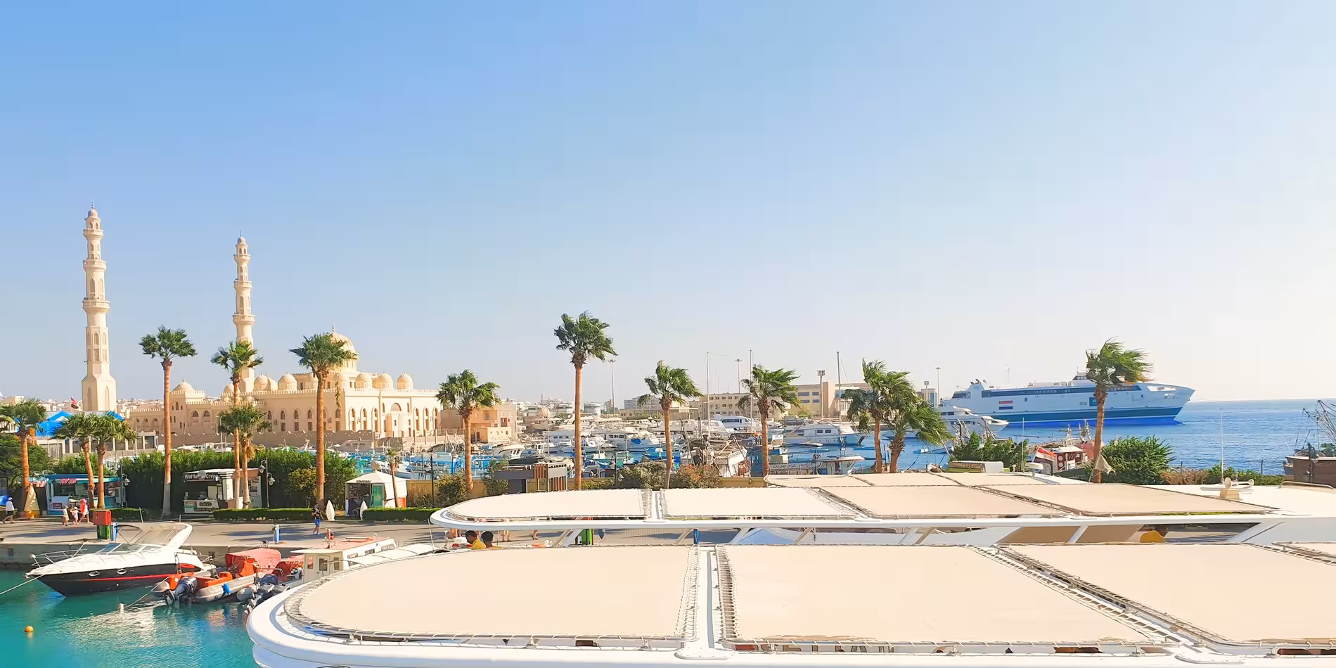 Hurghada old port marina with mosque minarets, palm trees, and cruise ship on Red Sea