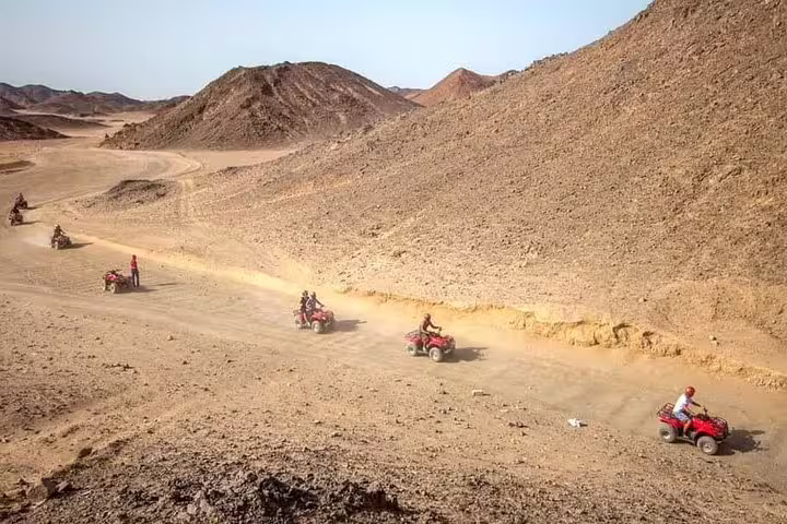 Quad bikes riding through rugged desert mountains on sunset safari trip, thrilling off-road route before Bedouin dinner