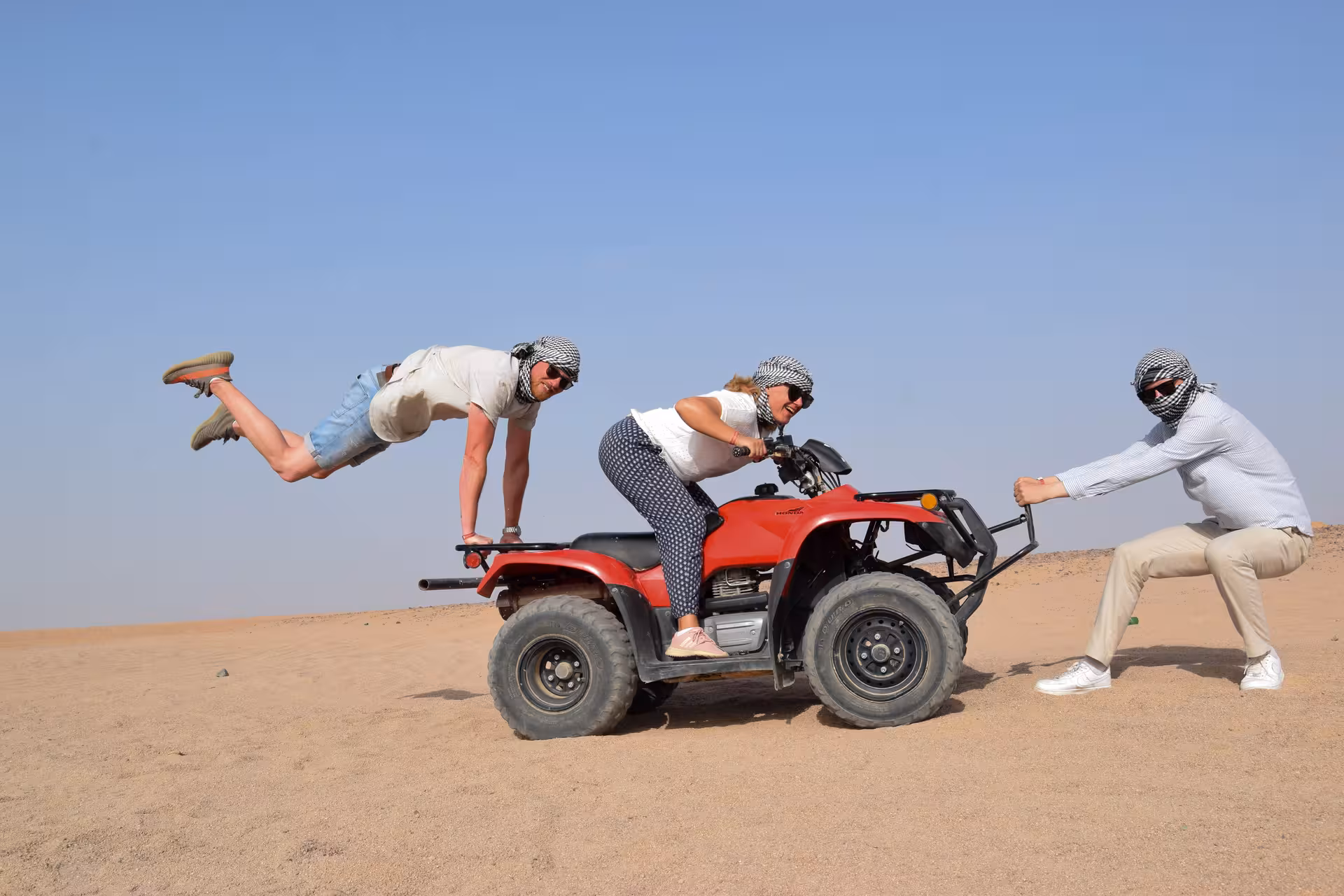 Playful group posing on red quad bike in Hurghada desert, action-packed ATV safari and Bedouin village trip