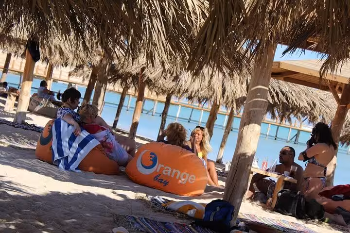 Guests lounging under palm huts on Hurghada Safaga beach, part of a 3-hour private fishing and snorkeling trip