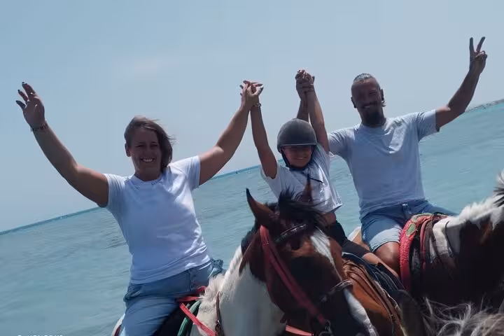 Happy riders raising hands during Hurghada sea horse riding tour, Red Sea shoreline adventure with optional swim