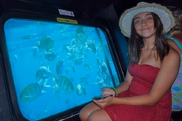 Woman inside Hurghada semi-submarine posing by large window with Red Sea fish and reef on 2-hour adventure