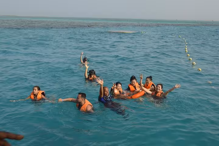 Guests snorkeling in the Red Sea from Hurghada semi-submarine tour, wearing life jackets and waving