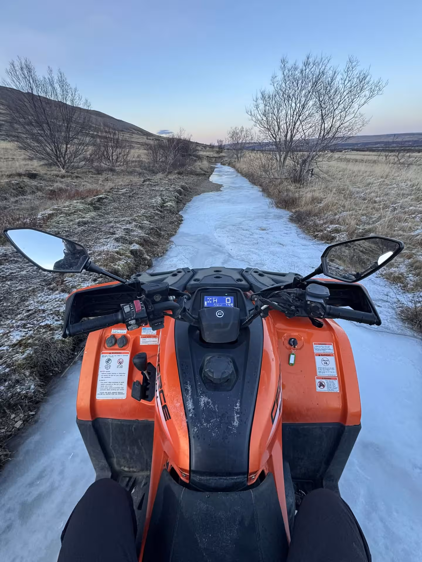 First-person view from orange ATV quad bike on icy trail through Husafell winter landscape