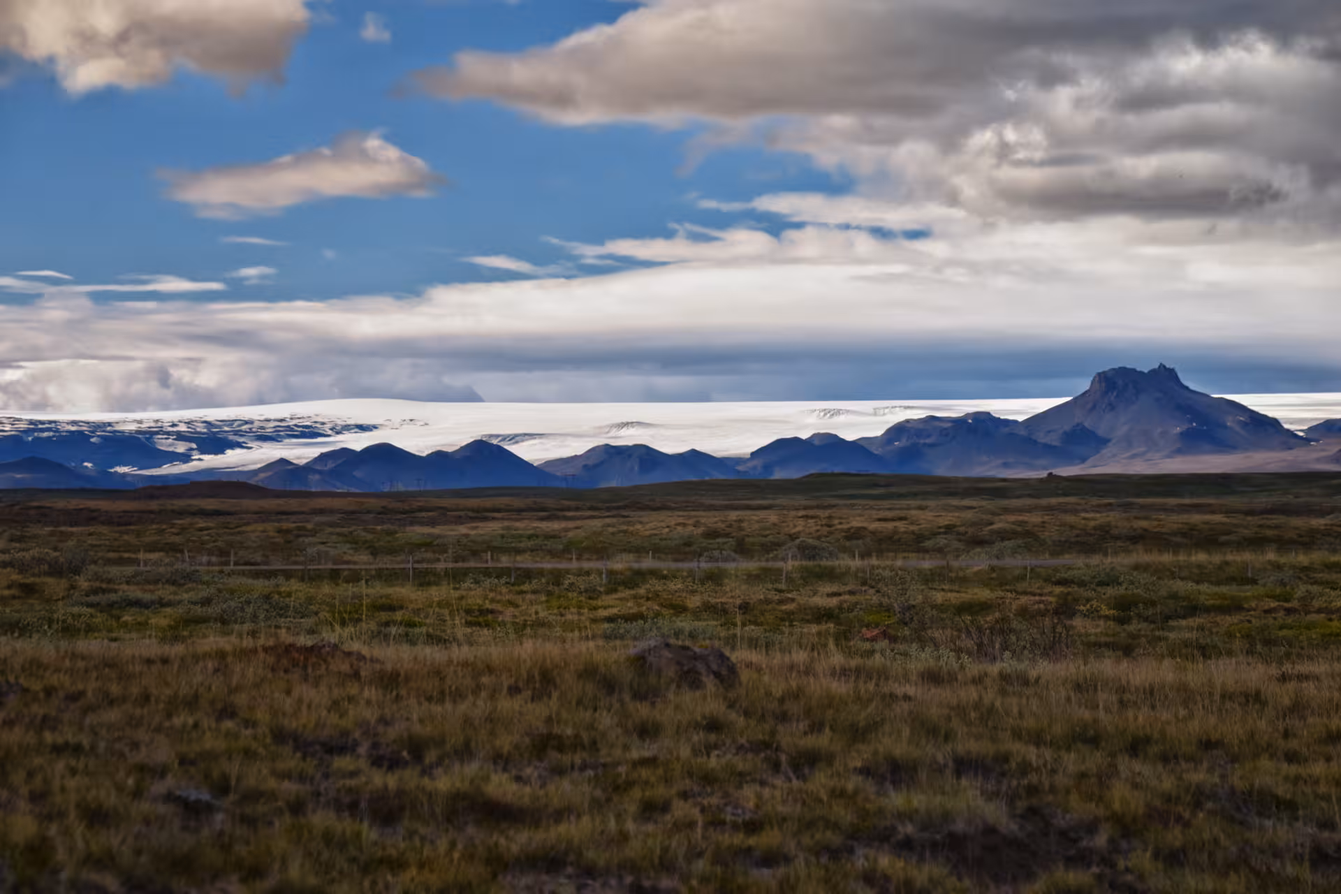 Vast Icelandic highland tundra with volcanic mountains and glacier in background under blue sky