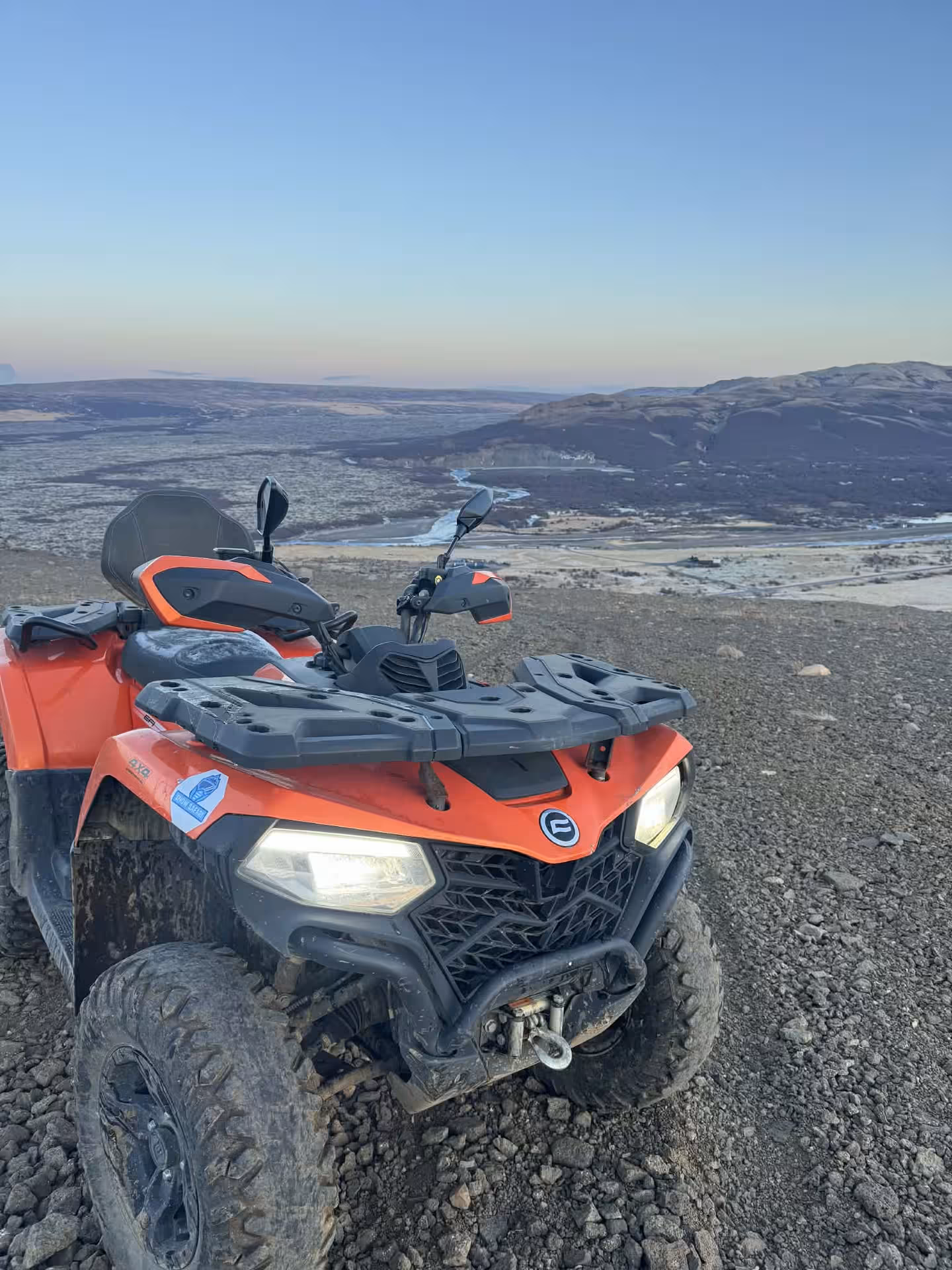Red ATV quad bike parked on rocky highland terrain with panoramic Husafell valley views at sunset