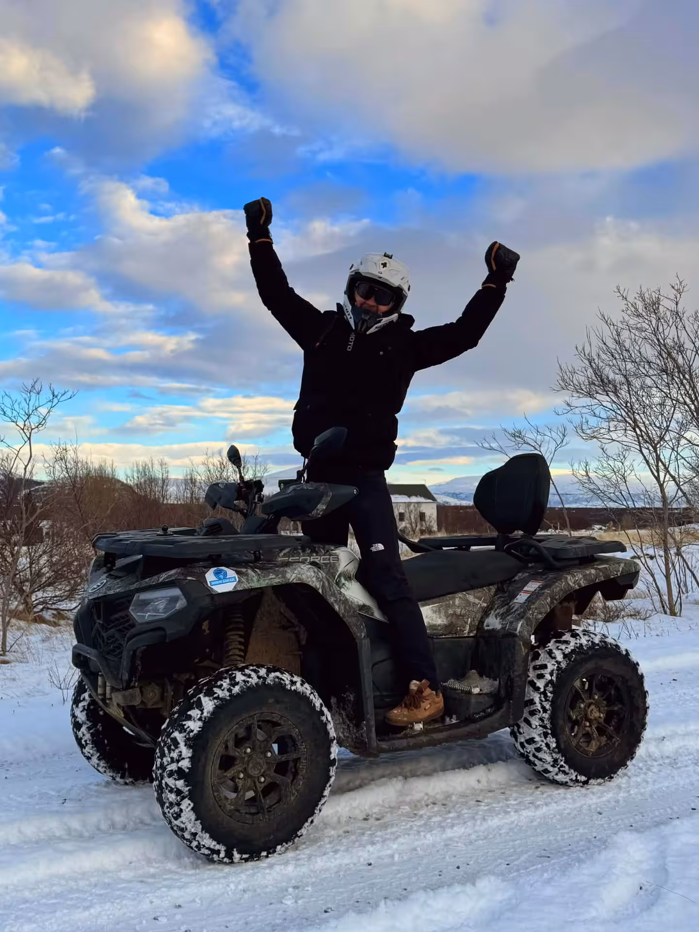 Person standing on ATV quad bike with arms raised in snowy Husafell winter landscape