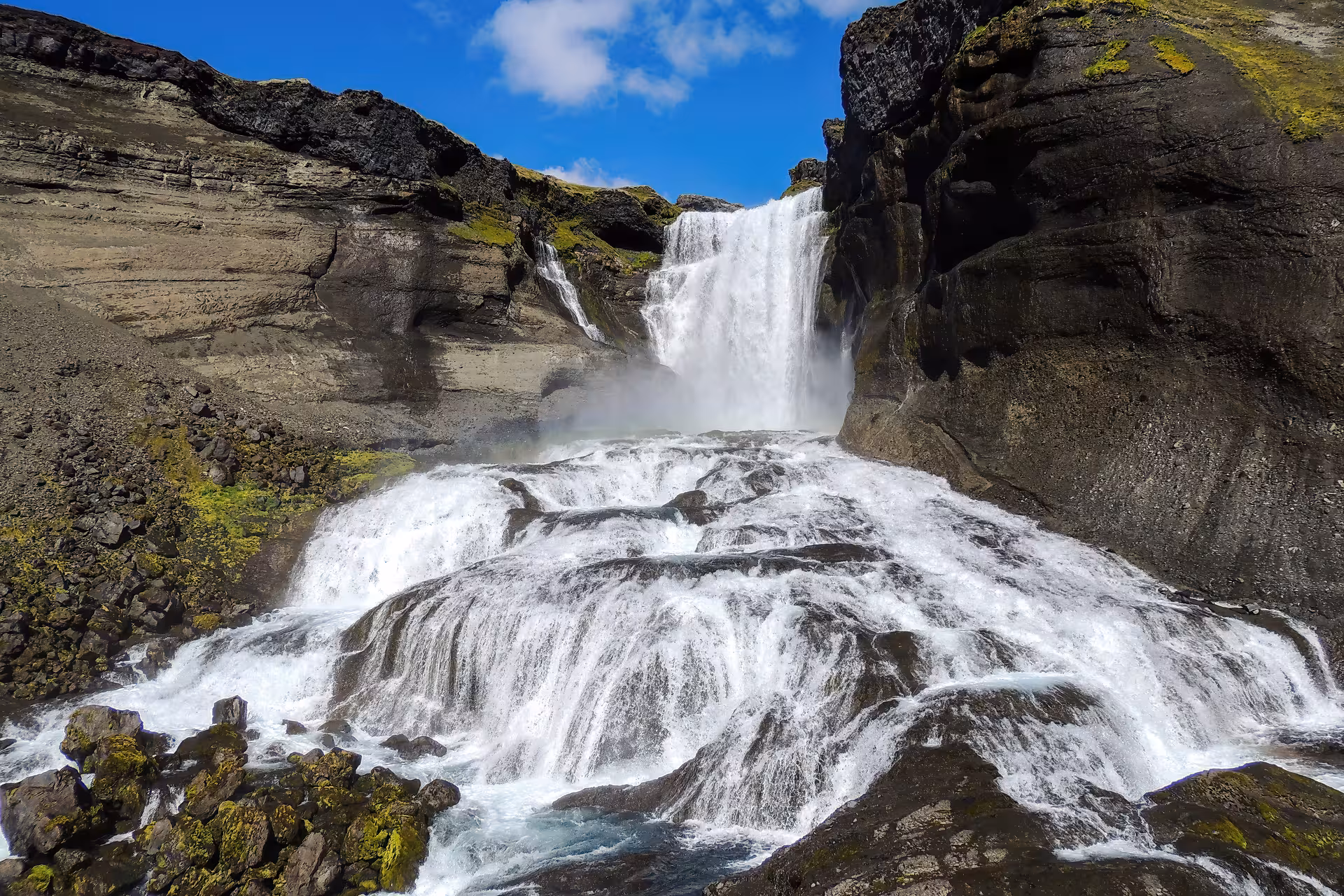 Powerful waterfall cascading over dark volcanic rocks with moss-covered cliffs near Husafell, Iceland