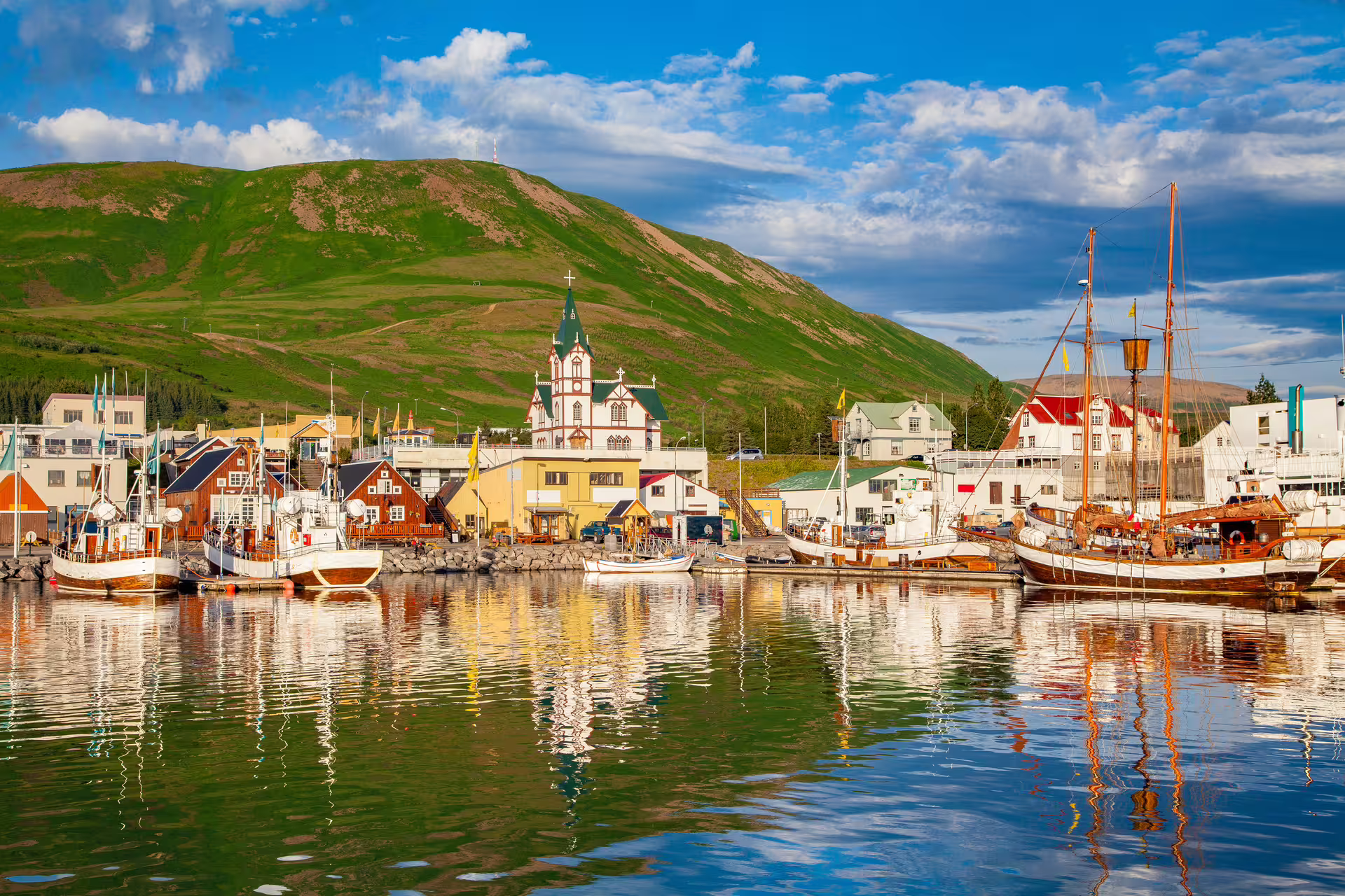 Husavik harbor with colorful boats, historic church, and green hillside on Iceland's Diamond Circle route